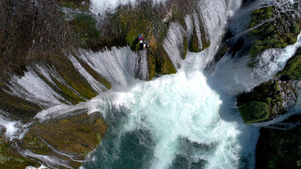 group of people doing white water rafting activity on wild river with waterfall