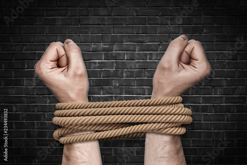 Fotomural Two bound strong male arms struggling to break a strong natural rope on a black brick background