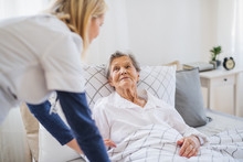 A Health Visitor Talking To A Sick Senior Woman Lying In Bed At Home.