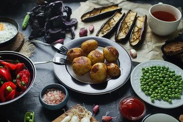 Delicious dinner table for two with fried potatoes, organic tomatoes salad, olives, green onion, eggplants, eggs on dark stone background.