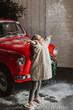 cute little girl standing next to a red car and a Christmas tree throws up snow