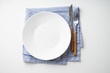 © Anastasiia Nurullina - White empty plate with knife and fork on striped blue and white textile napkin on white background