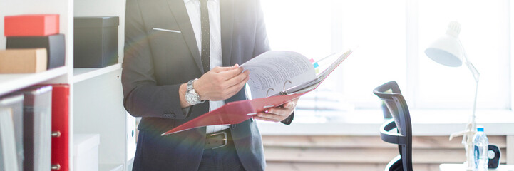 Wall Mural - The man is standing near the rack in the office and scrolls through the folder with the documents.