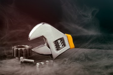 Adjustable wrench with nuts and screw wrapped in steam on black background