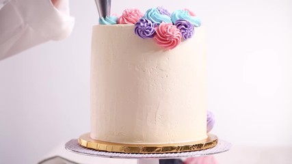 Wall Mural - Baker piping pastel color buttercream rosettes on a white cake to make a unicorn cake.