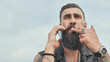 © Довидович Михаил - Brutal bearded man talking on the phone and smokes a cigarette.