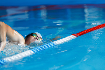 Wall Mural - Photo of sports man in blue cap swimming in pool