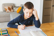 © laniko - Schoolboy doing his homework on desk at home.