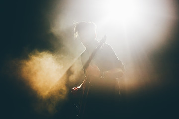 Guitarist silhouette on a stage in a backlights in the smoke playing rock music