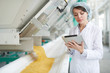 © Seventyfour - Waist up portrait of  young woman standing by machines and using digital tablet while inspecting macaroni production at food factory , copy space