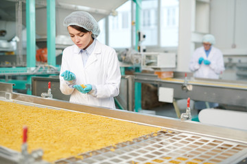 Wall Mural - Portrait of pretty young woman working at modern food factory and  inspecting macaroni on production line, copy space