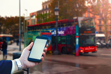 Mockup Of The Smartphone In The Hand Of A Guy Against The Background Of A Tourist Bus In Barcelona.