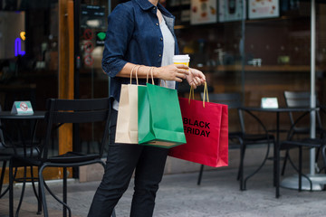 Black friday. Woman with coffee cup in hand, holding shopping bag while walking on the shopping mall background.