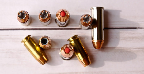 Six 40 caliber hollow point bullets along with three 44 special red tipped bullets shot from above on a white wooden background