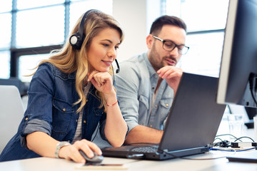 Female call center operator working with her headset on. Supervisor is sitting next to her.