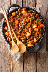 Wall Mural - Delicious Picadillo cooked from ground beef with vegetables, raisins and spices close-up in a frying pan. Vertical top view