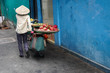 Vietnamese fruit vendor woman wears conical hat pushes bicycle sells exotic dragon fruit in an empty alleyway with bright walls