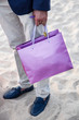 Busta viola tenuta in mano da uomo elegante in spiaggia