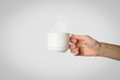Female hand holding a white cup with hot coffee on a gray background. Side view