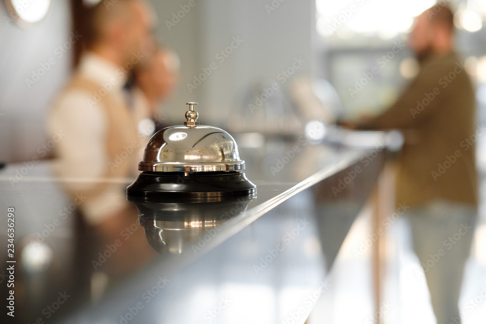 Modern luxury Hotel Reception Counter desk with Bell. Service Bell locating at reception. Silver Call Bell on table, Receptionists and customer on background. Сheck in hotel. Concept. - obrazy, fototapety, plakaty 