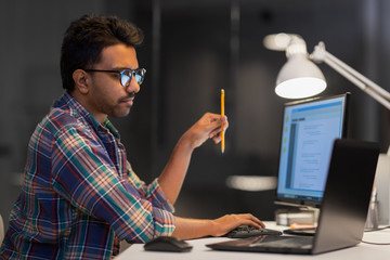 deadline, technology and people concept - creative man in glasses working with laptop computer at ni