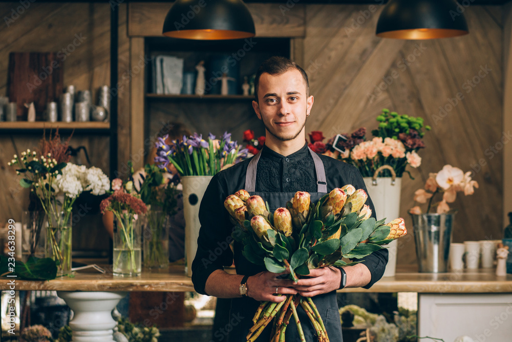 Man florist holding a protea flowers arrangements in modern interior floral shop. Small business, welcoming concept. - obrazy, fototapety, plakaty 