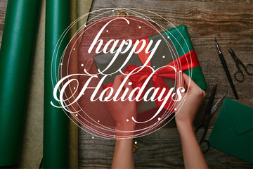 Canvas Print - cropped shot of woman tying ribbon on christmas present on wooden tabletop with wrapping paper, 