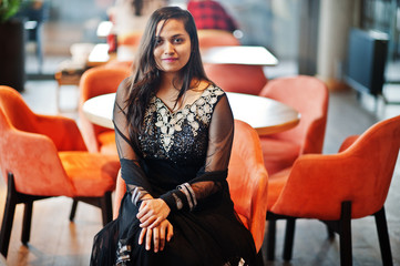 Pretty indian girl in black saree dress posed at restaurant.