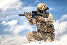 Fully Equipped With Tactical Ammunition Airsoft Player In Military Camouflage Uniform, Aiming With Optical Sight On Service Assault Rifle Replica While Stand On One Knee At Cloudy Sky Background
