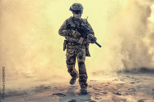 Cuadros en Lienzo Army soldier in military camouflage uniform, helmet, with face hiding behind mask and glasses, running out from fire