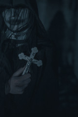 Woman is standing in a darkness with a cross in her hand in an image of a nun possessed by demons.