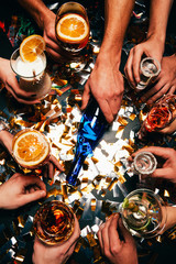 partial view of friends with various alcoholic cocktails playing spin the bottle at table covered by golden confetti