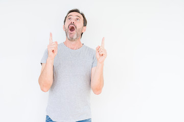 Handsome senior man over isolated background amazed and surprised looking up and pointing with fingers and raised arms.