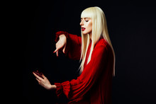 Portrait Of A Beautiful Blonde Woman Looking Down At A Red Smartphone About To Press The Button, Isolated On Black Studio Background