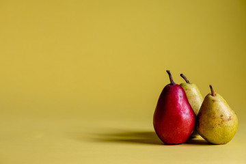 Two green pears and one red pear on a yellow background.