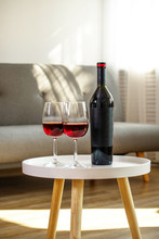 Vintage Bottle Of Red Wine With Blank Matte Black Label On Table With Two Glasses In Empty Loft Living Room. Expensive Bottle Of Cabernet Sauvignon Concept. Copy Space, Top View, Close Up.