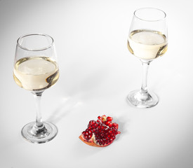 Broken pomegranate lies on a white plate. Two glasses of white wine.