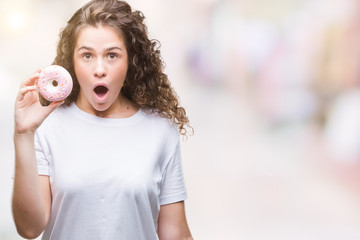 Wall Mural - Young brunette girl eating donut over isolated background scared in shock with a surprise face, afraid and excited with fear expression