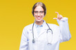 © Krakenimages.com - Beautiful young blonde doctor woman wearing medical uniform over isolated background smiling and confident gesturing with hand doing size sign with fingers