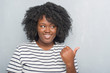 © Krakenimages.com - Young african american plus size woman over grey grunge wall smiling with happy face looking and pointing to the side with thumb up.