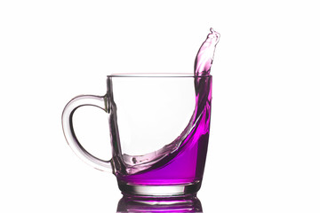 Transparent mug with purple liquid pouring out, isolate, close-up