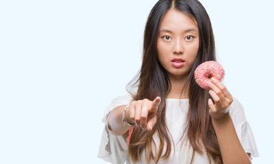 Wall Mural - Young asian woman eating donut over isolated background pointing with finger to the camera and to you, hand sign, positive and confident gesture from the front