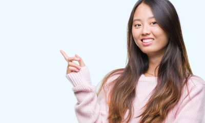 Young asian woman over isolated background with a big smile on face, pointing with hand and finger to the side looking at the camera.