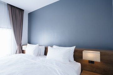 Close-up of white pillow on bed decoration with light lamp in hotel bedroom interior.