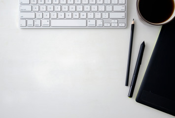 White wooden table with keyboard, graphics tablet, pen, pencil and a cup of black coffee. Workspace top view with copy space.