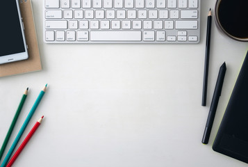 White wooden table with keyboard, graphics tablet, pen, black and color pencils, craft notebook, cell phone and a cup of coffee. Workspace top view with copy space.