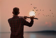© ittipol - Man playing flute with sunset or sunrise background