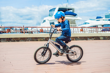 Wall Mural - Happy kid boy having fun near the yacht club with a bicycle on beautiful day. Active child wearing bike helmet