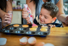 Mother Helping Son To Put Frosting Onto Cupcakes