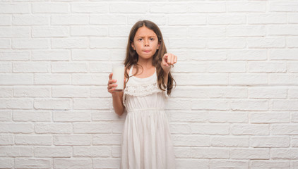 Sticker - Young hispanic kid over white brick wall drinking a glass of milk pointing with finger to the camera and to you, hand sign, positive and confident gesture from the front